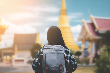 Backpack woman standing front of blur temple Thailand with blue sky and white cloud background.
