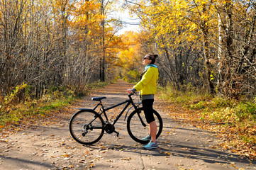 Obraz na płótnie Canvas Girl with a bicycle on the road among autumn forest