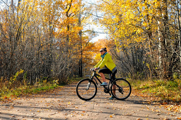 Fototapeta premium Girl with a bicycle on the road among autumn forest
