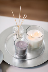 decoration, hygge and aromatherapy concept - aroma reed diffuser an candles burning on tray