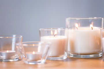 decoration, hygge and cosiness concept - burning white fragrance candles on wooden table