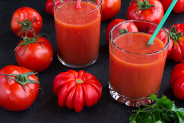 Two glasses of tomato juice among tomatoes on a black background