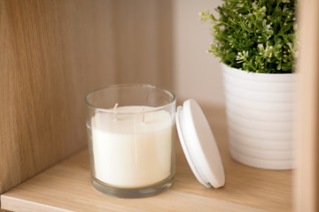 decoration and interior concept - white fragrance candle in glass holder and pot flower on wooden shelving at home