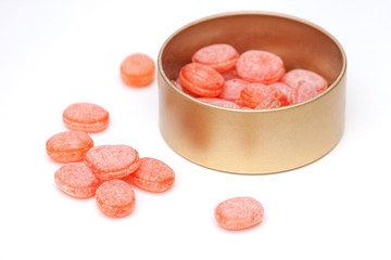 Orange candies in tin jar on white background.