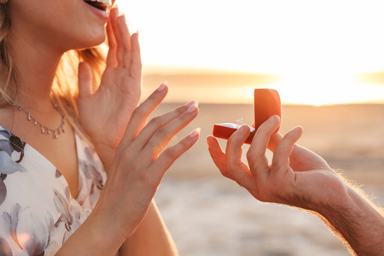 Cropped photo of romantic caucasian man making proposal to his girlfriend with ring walking on sunny beach