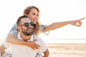 Photo of unshaven cheerful man smiling and giving piggyback ride seductive woman while walking on...