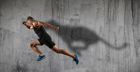 Fototapeta na wymiar Athletic man sprinter running on dark wall background