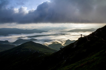 Wide mountain panorama. Small silhouette of tourist with backpack on rocky mountain slope with...