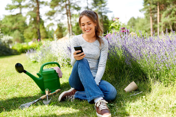 gardening, technology and people concept - happy young woman or gardener with smartphone and garden...