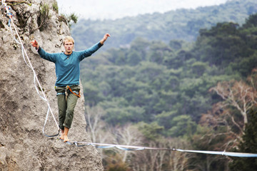 A man is walking along a stretched sling. Highline in the mountains. Man catches balance. Performance of a tightrope walker in nature. Highliner on the background of the mountains.