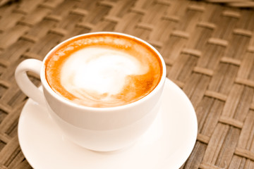 Cappuccino in white cup on wood table background at cafe. Place for text. Bewerages, coffee lovers and morning menu concept. Stylish toning.