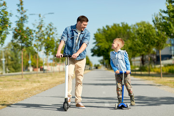 Fototapeta premium family, leisure and fatherhood concept - happy father spending time with little son riding scooters in city