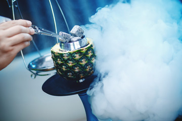 Hookahman changes coals for hookah with tweezers, bowl of pineapple blue