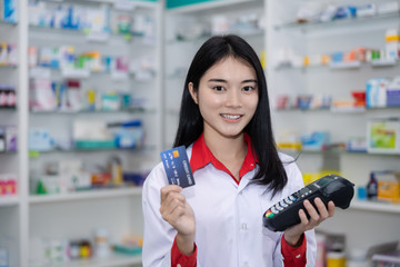 asian female pharmacist in pharmacy and credit card machine health care and digital payments concept