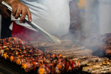 Chef preparing meat on a charcoal grill, pork steaks, chicken breast, sausages, pieces of meat chops at a street food festival