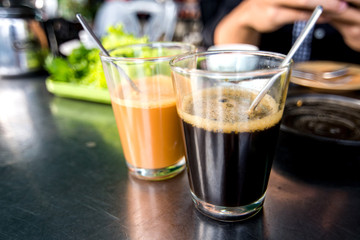 Black coffee and milk tea in transparent glass on stainless table in breakfast restaurant.
