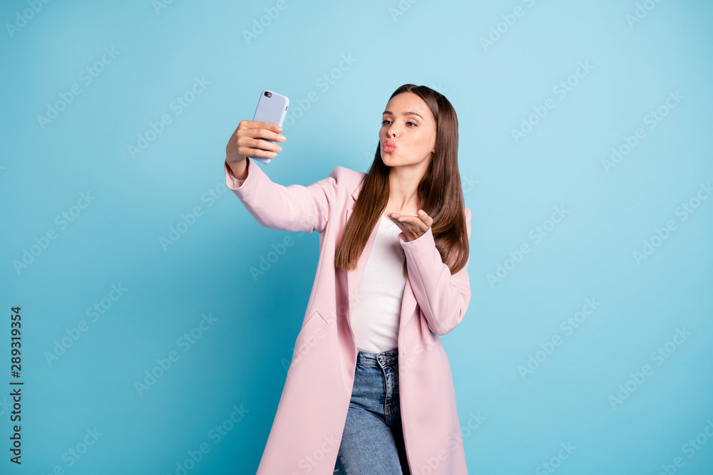 Sticker Portrait of cute charming lady sending air kisses to her boyfriend taking selfie wearing topcoat denim jeans isolated over blue color background