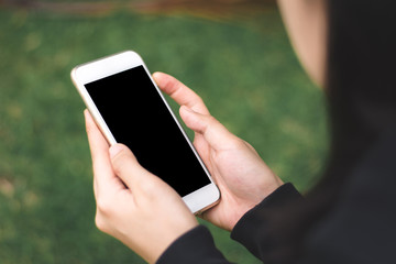 Close up of woman hands using mobile smart phone with blank screen against green grass background.