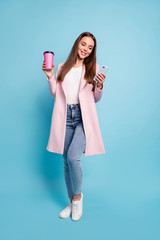 Full size photo of cute lovely girl using her cell phone reading news wearing denim jeans topcoat isolated over blue background