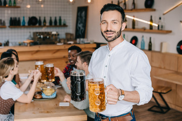 handsome young man holding mugs of light and dark beer and smiling at camera