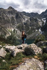 Fototapeta na wymiar Young girl traveler in red sportswear removes a backpack among the mountains on the background of lake