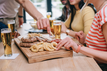 partial view of multicultural friends sitting at pub near tray with fried onion rings, sausages and french fries