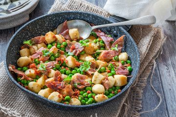 Potato gnocchi with green peas, pesto, proscuitto and chorizo in frying pan