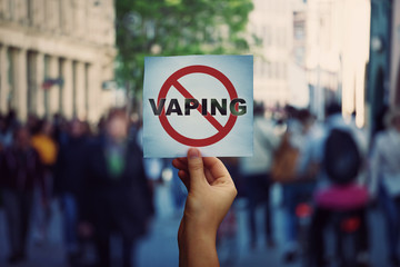 Human hand holding a protest banner stop vaping message over a crowded street background. Banning flavored vaping products to discourage people from smoking electronic cigarettes. Health risk concept. - 289322970