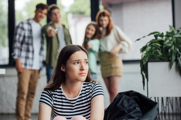 selective focus of group of teenagers bullying sad girl in school - obrazy, fototapety, plakaty
