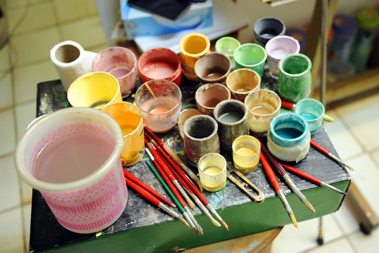 Muchos pinceles y frascos de vidrio con pigmentos de colores cer&aacute;micos preparados para pintar azulejos a mano en el taller de alfarer&iacute;a
