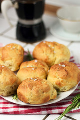 homemade fresh herb bread rolls of Provencal herbs with salt and sprig branch of rosemary. Bread rolls bakery style on white plate and red white towel cage italian style, black geyser coffee machine