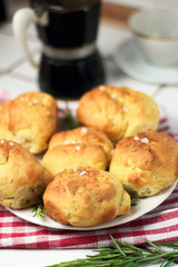 homemade fresh herb bread rolls of Provencal herbs with salt and sprig branch of rosemary. Bread rolls bakery style on white plate and red white towel cage italian style, black geyser coffee machine