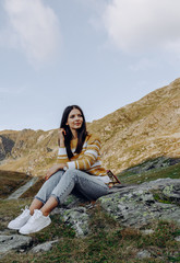 Naklejka premium Stylish girl in rustic dress smiling and waving hair in sunny meadow in mountains. Portrait of happy boho woman in countryside at sunset, positive vibes, rural simple life. Atmospheric image