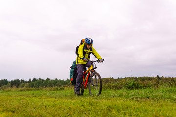 bikepacker looks at the road while riding across the field in the rain