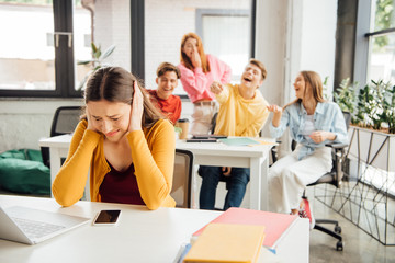 sad girl covering ears with hands while classmates bullying her
