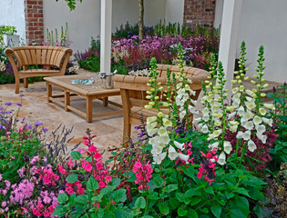 A contemporary garden with terraced area and stylish wooden furniture surrounded by colourful...