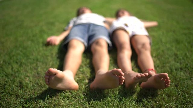 Closeup, barefoot little boy and girl lying on the lawn and moving feet. Closeup shot, soft focus.