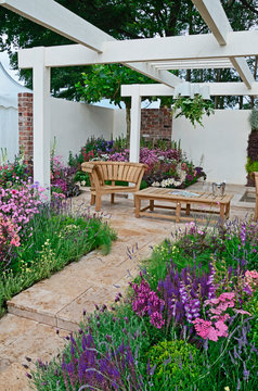A contemporary garden with terraced area and stylish wooden furniture surrounded by colourful flowering borders