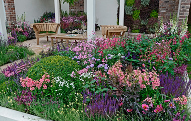 Fototapeta premium A contemporary garden with terraced area and stylish wooden furniture surrounded by colourful flowering borders