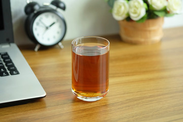 Tea in a clear glass on a wooden office desk with a laptop computer, Tea afternoon break