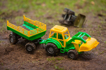 The toy tractor is working. Green and yellow tractor with a trailer. Tractor with a bucket, toy.