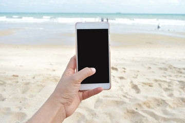 woman hand holding smart phone on beach background.