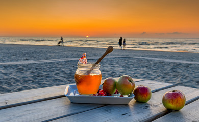 Honey, apples and pomegranate are symbols of Jewish New Year holiday - Rosh ha - Shanah.  Festive food  attributes are laying on wooden table, background with blurred defocused sea and sunset