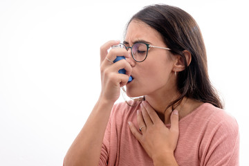 Young caucasian brunette girl with pink shirt suffers from asthma inhaling with an inhaler. isolated in white background.