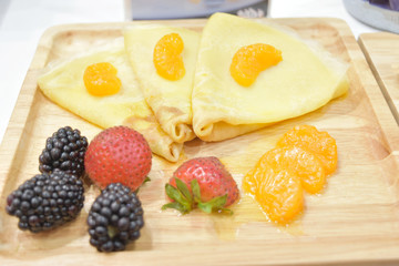 Fresh pancakes with strawberry, black berries and orange on wooden plate.