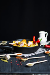 spicy fried potatoes with bacon in a pan and various spices on a dark background