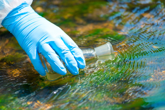 close up of a scientist's river drawing water into a research flask from a stream