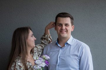 Happy couple in a good mood joking with each other. Smiling faces. Girl touches a guy by the ear. Grey background.