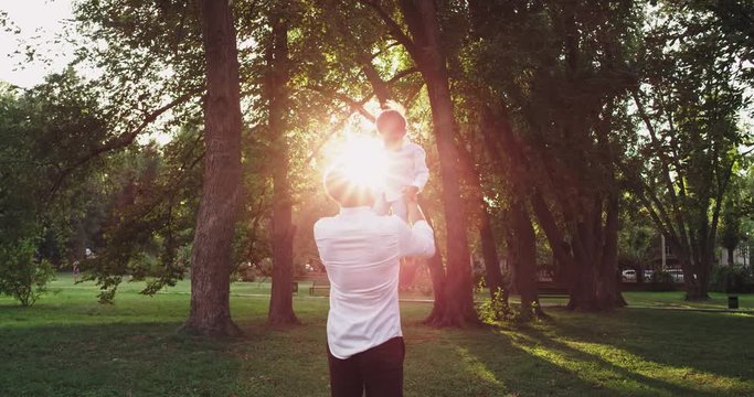 Cute small boy with his dad playing very lovely at sunset in the middle of green park enjoying the moment together wearing a stylish clothes
