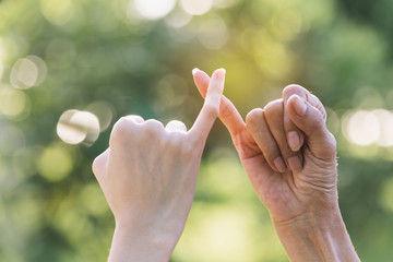 Closeup two person hook each other's little finger on nature background.